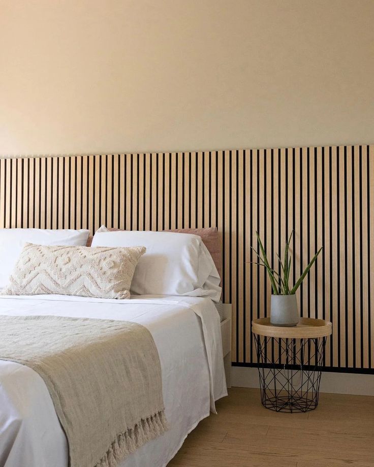 a white bed sitting in a bedroom next to a wooden table with a potted plant on it