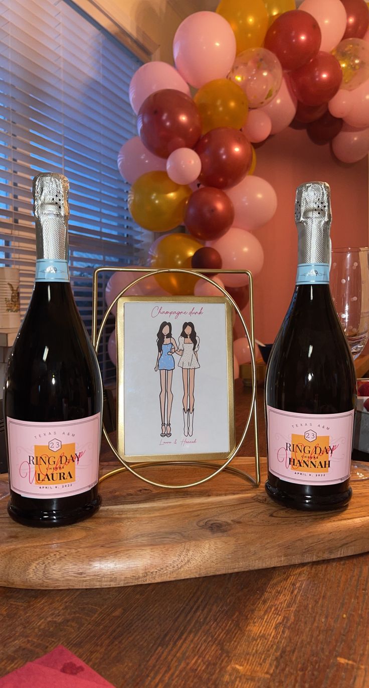 two bottles of wine sitting on top of a wooden table with balloons in the background