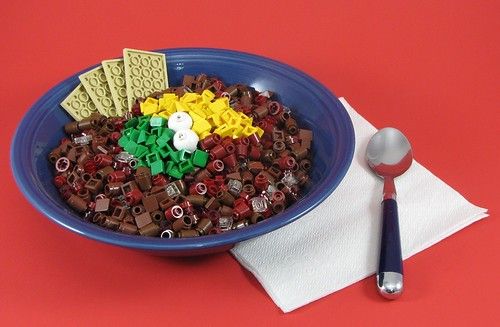 a blue bowl filled with lots of legos on top of a white napkin next to a spoon