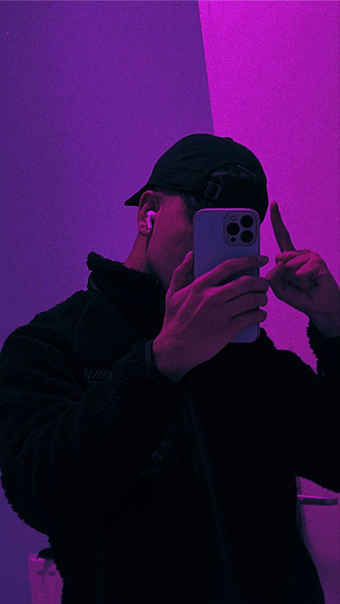 a man taking a selfie in front of a purple and pink wall with his cell phone