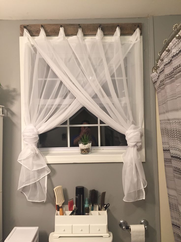 a white toilet sitting under a window next to a bathroom sink with a curtain over it