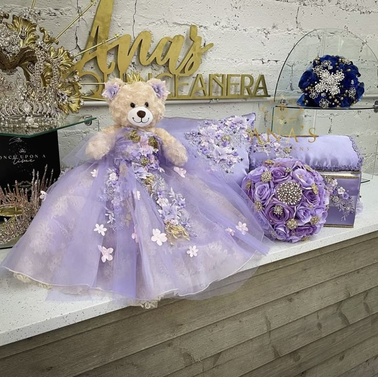 a teddy bear sitting on top of a counter next to purple flowers and other items