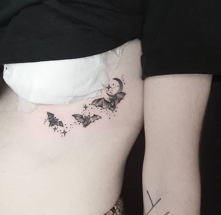 a woman's lower back tattoo with butterflies on her ribs and the moon in the sky