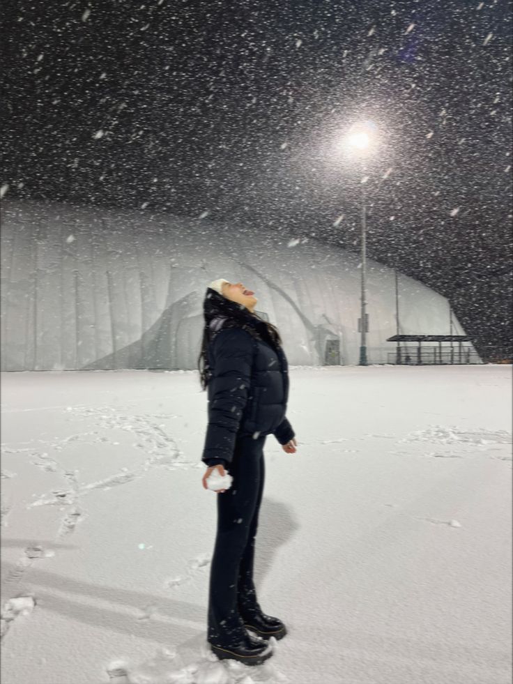 a woman standing in the snow at night with her back turned to the camera and looking into the distance