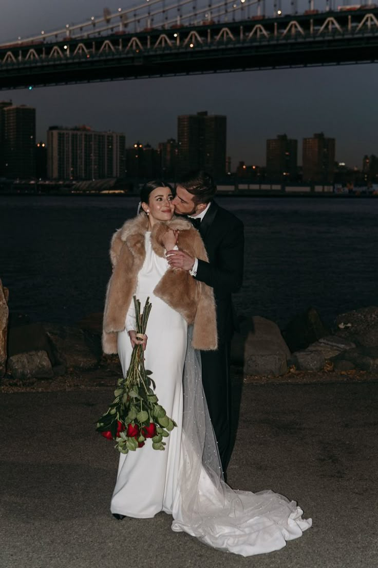 a bride and groom are standing in front of the water under a bridge at night