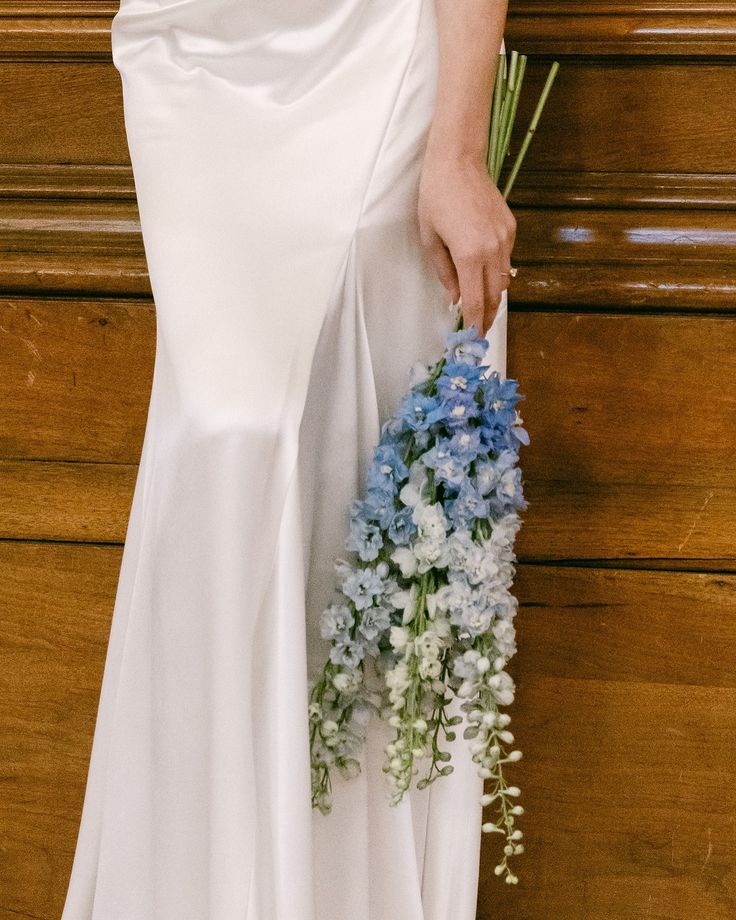 a woman in a white dress holding a bouquet of flowers next to a wooden wall