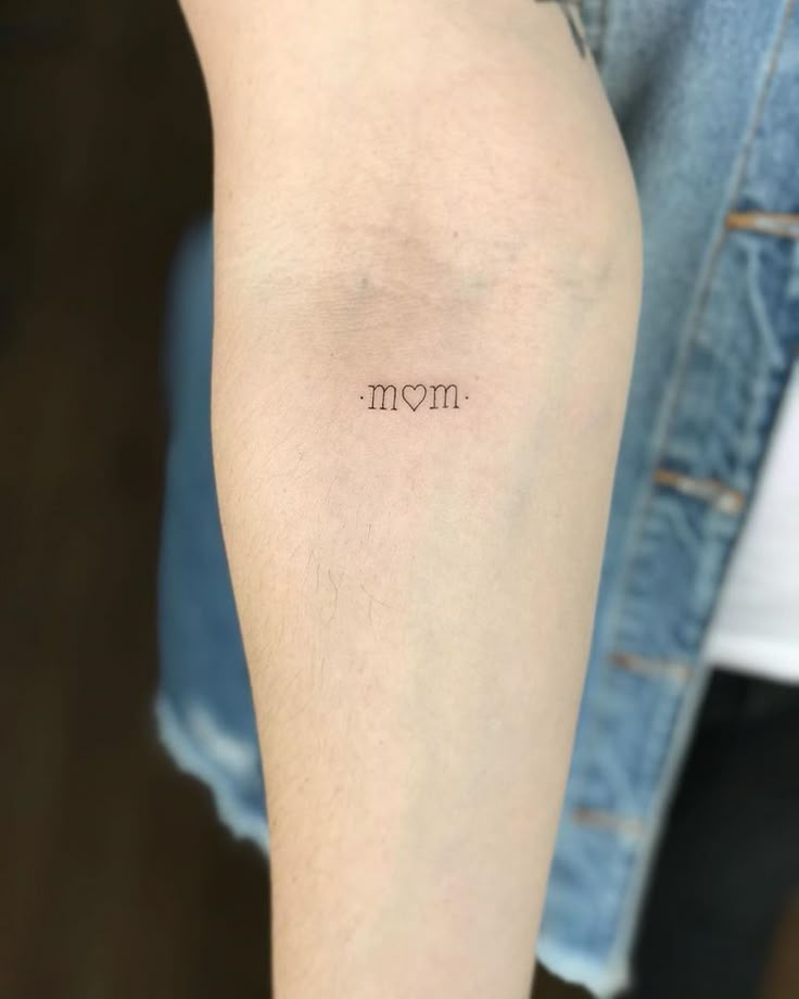 a woman's arm with the word mom tattooed on her left arm, in small font