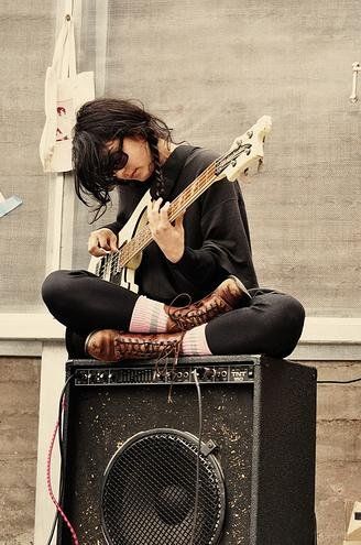 a woman sitting on top of an amp with a guitar in her lap and wearing tight black leggings