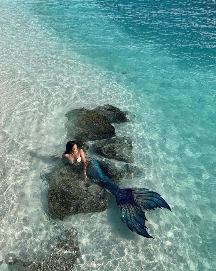 a woman laying on top of a rock in the ocean next to some rocks with a mermaid tail