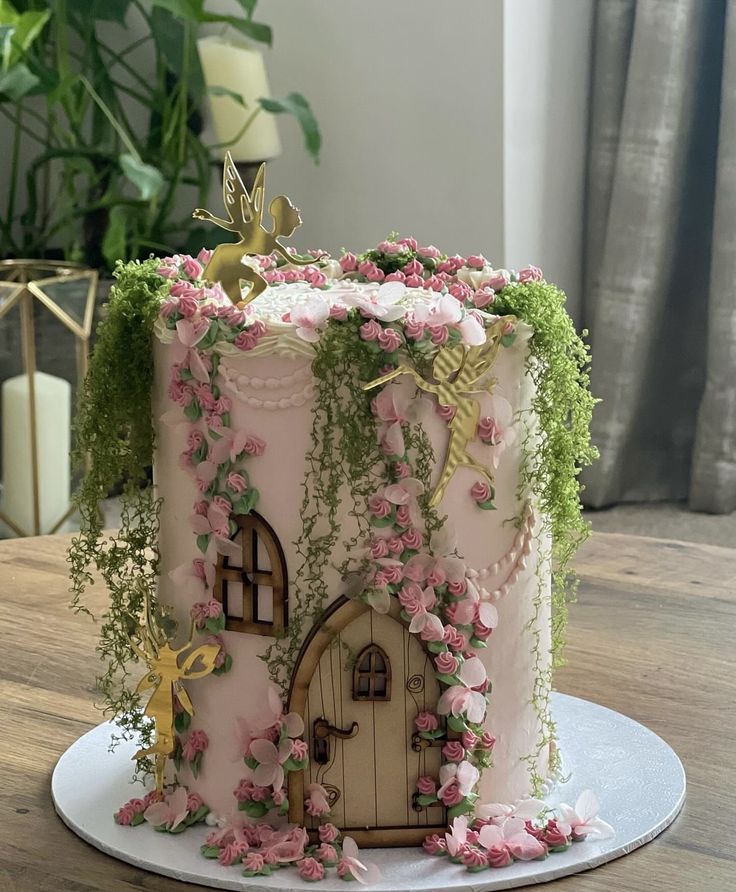 a cake decorated with pink flowers and vines on a table next to a potted plant