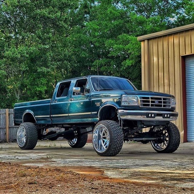 a large green truck parked in front of a blue garage door with trees behind it