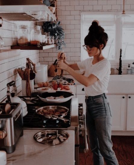 a woman standing in a kitchen preparing food on top of a stove next to a sink