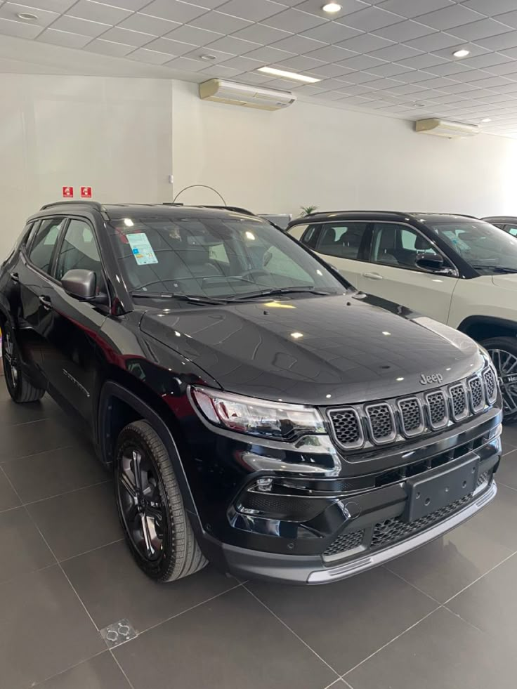 two jeeps are parked in a showroom next to each other and one is black