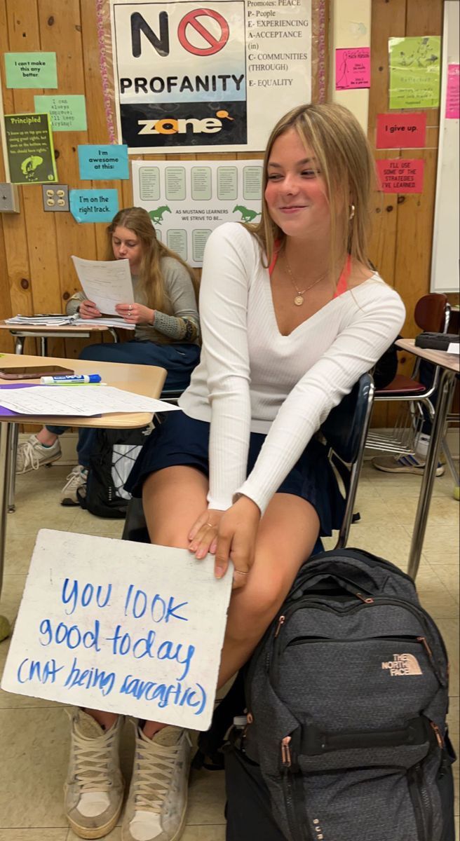 a woman sitting in a classroom holding a sign that says you look good today