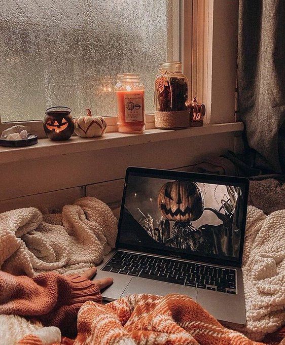 an open laptop computer sitting on top of a bed next to candles and pumpkins