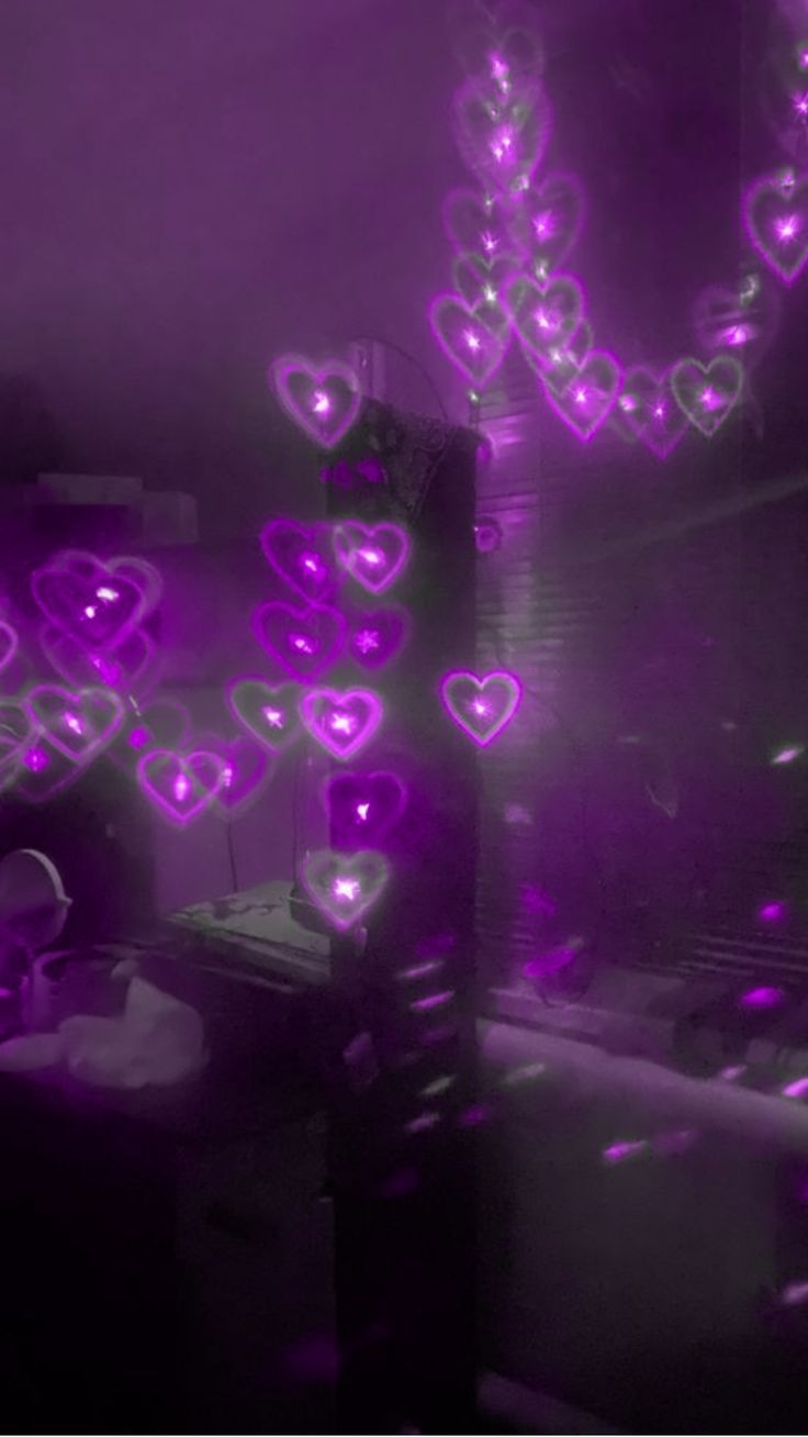 purple lights in the shape of hearts are shining on a dark room with a desk and chair