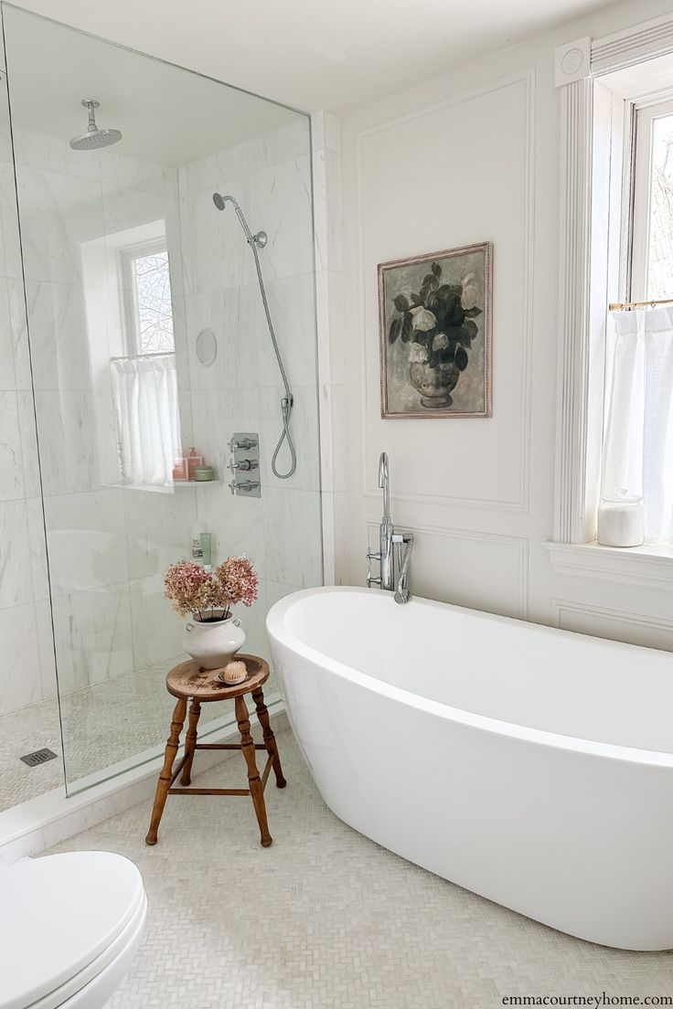 a white bathtub sitting next to a window in a bathroom with a wooden stool