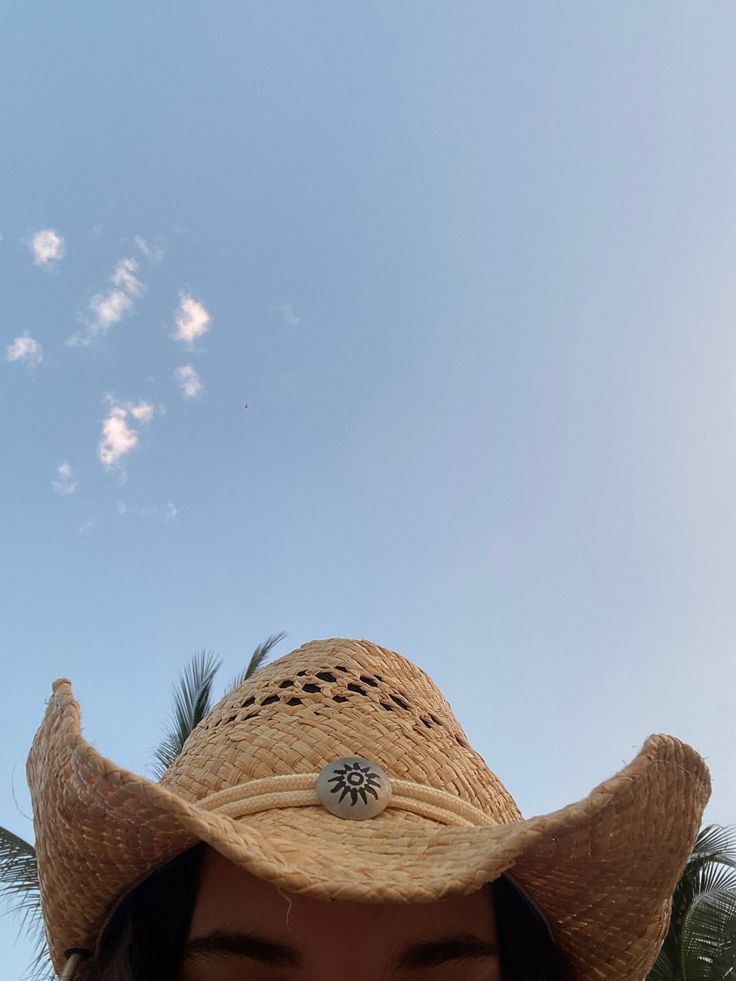 a woman wearing a straw hat and looking up at the sky with palm trees in the background