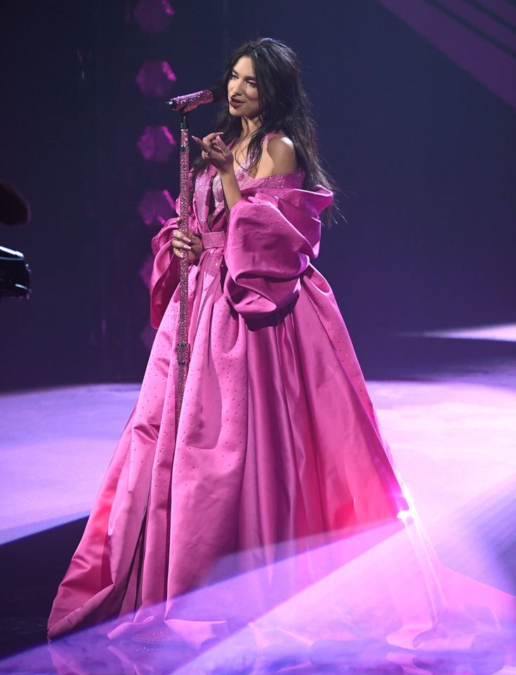 a woman in a long pink dress on stage with a microphone and lights behind her