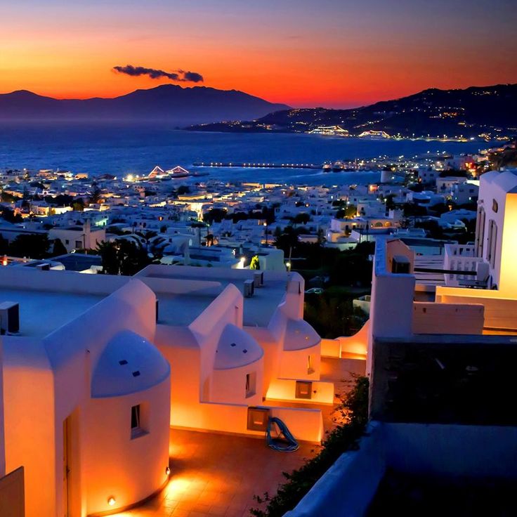 the city lights are lit up at night in front of an ocean and mountain range