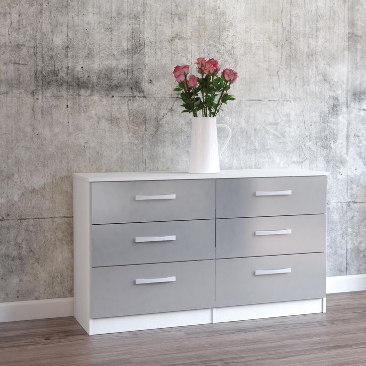 a vase with flowers on top of a white dresser next to a chair and wall