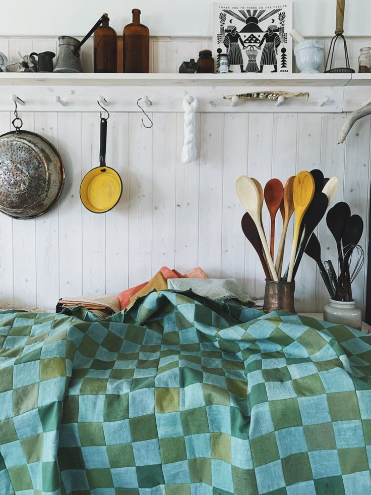 kitchen utensils are lined up on the wall next to a green checkered bedspread