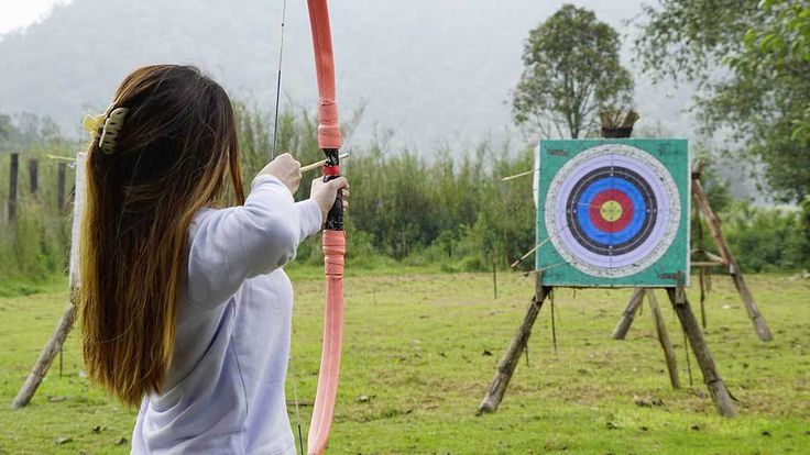 a girl is aiming an arrow at a target in the grass with mountains in the background