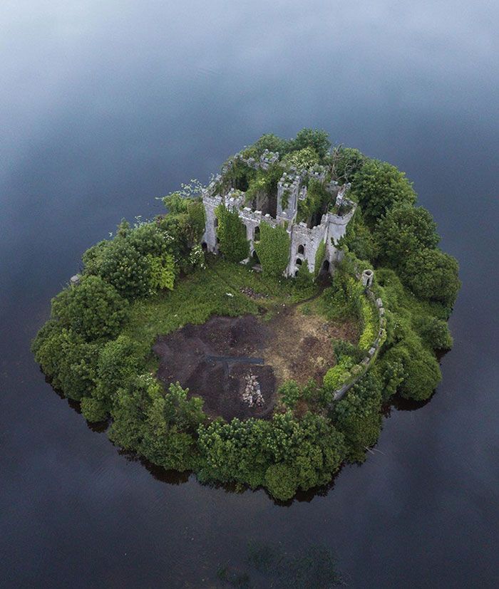 an island in the middle of water with a castle on it's side and trees around it