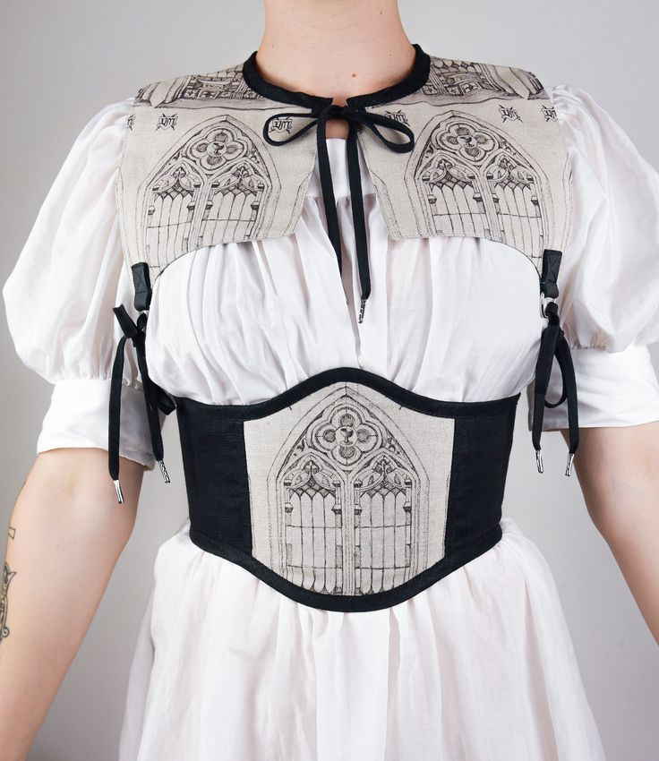 A corset-belt of midnight black linen featuring a single front panel of a Gothic cathedral window against an oatmeal background.Inspired by the ethereal elegance of medieval architecture & Victorian gothic aesthetics. This piece laces up at the center back through black steel eyelets. The exterior is made from new linen (a sustainable textile) while the lining is made from upcycled fabric. Pictured with the Silk Chemise and the Cathedral PartletAvailable in Small, Medium, Large and Extra Lar Victorian Belt, Architecture Victorian, Dramatic Dress, Goth Outfit Inspo, Wearable Sculpture, Belt Corset, Dramatic Dresses, Wedding Corset, Ethereal Elegance