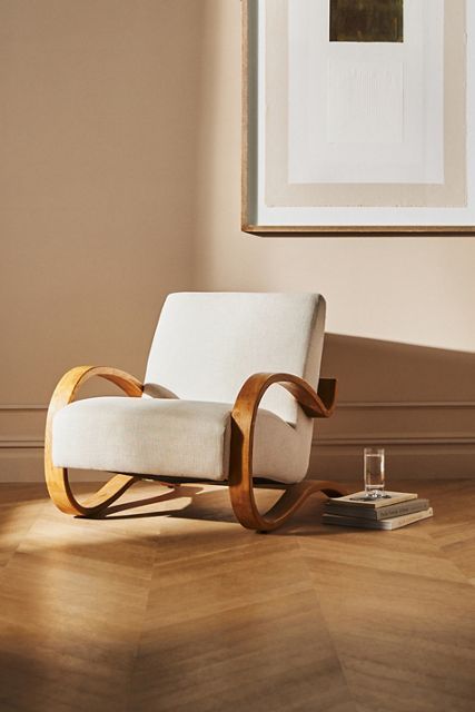 a white chair sitting on top of a hard wood floor next to a framed painting