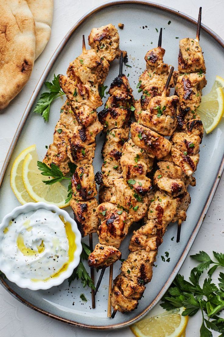 grilled chicken skewers with lemon wedges and sour cream sauce on a platter