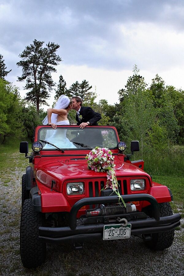 a bride and groom kissing on top of a red jeep