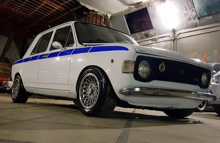 a white and blue car parked in a garage next to another car on the ground