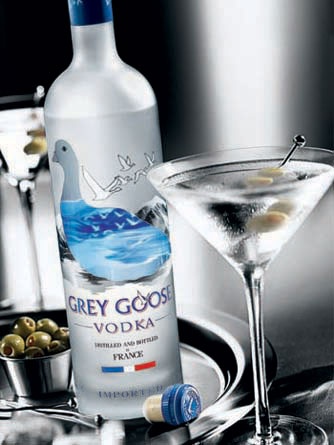 a bottle of grey goose vodka next to a martini glass with olives in it