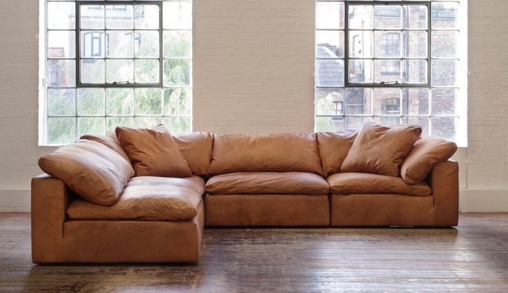 a brown leather sectional sofa in front of two windows