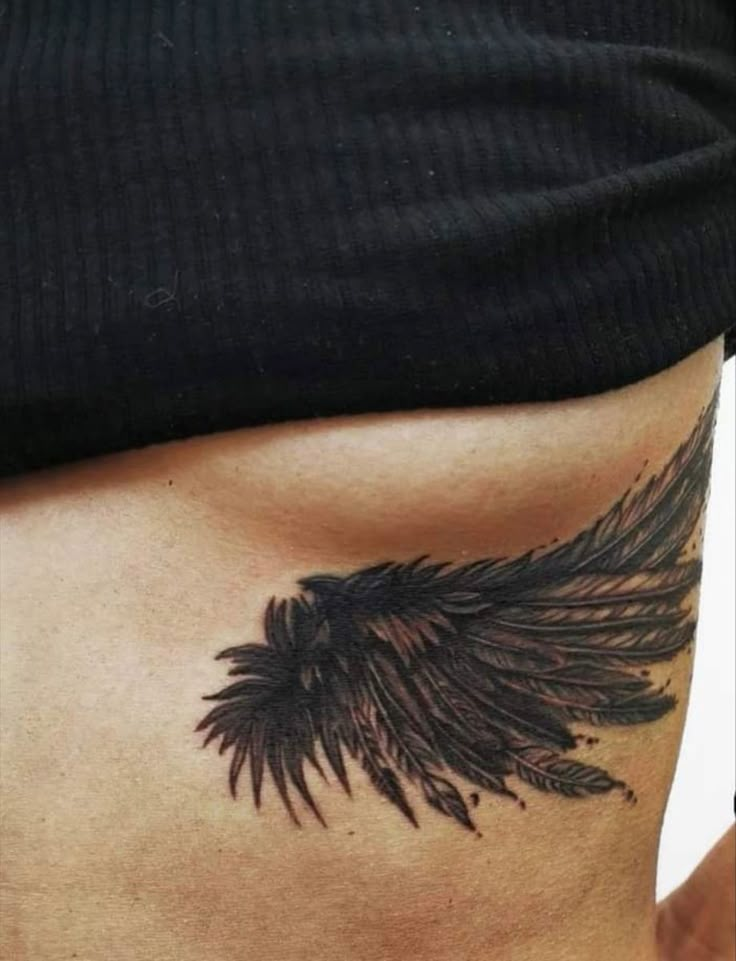 a woman's stomach with a black tattoo on her belly and an angel wing