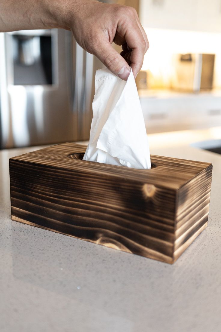 a person holding a tissue in front of a wooden box on a counter top with a microwave behind it