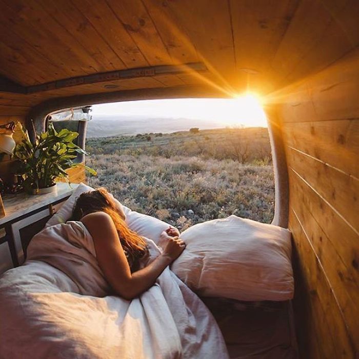 a woman laying in bed looking out the window at an open field with grass and flowers