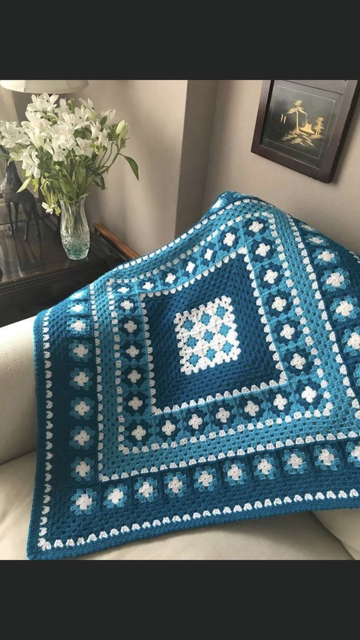 a blue crocheted blanket sitting on top of a couch next to a vase with flowers