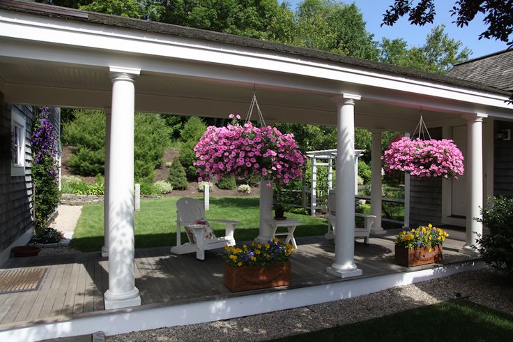 the porch is covered with white pillars and flower pots filled with pink petunias