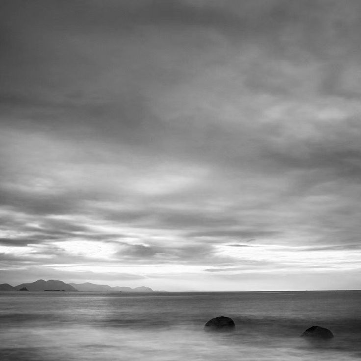 black and white photograph of the ocean with rocks in the foreground under a cloudy sky