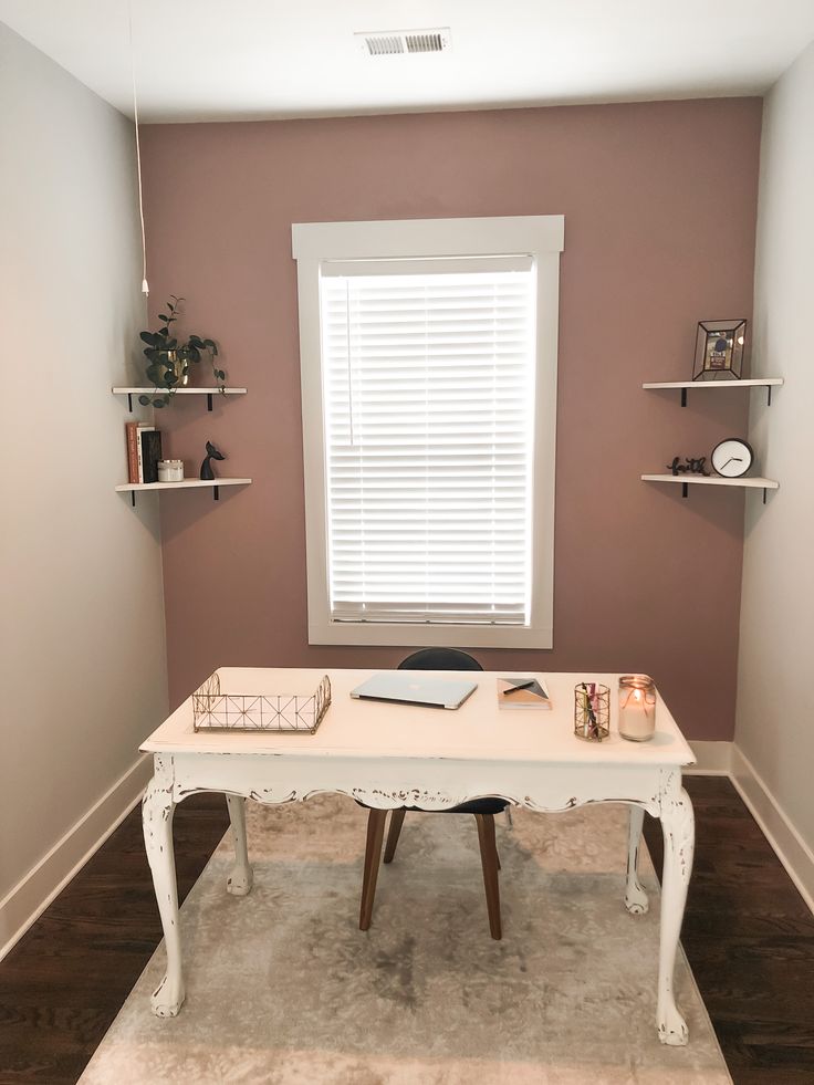 a room with a white desk and shelves on the wall, along with a window