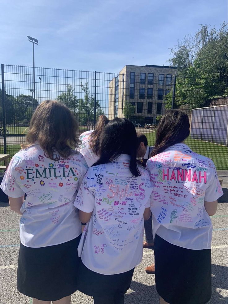 three girls in white shirts with writing on their backs are standing next to each other