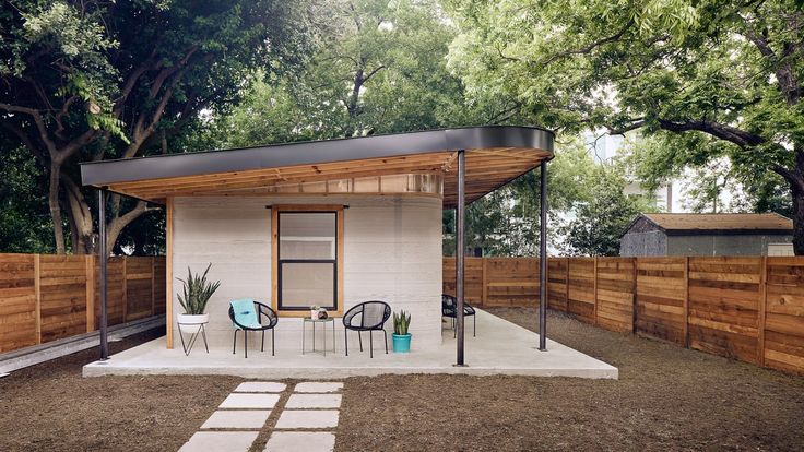 a small white house with a black roof and some chairs in the yard next to it