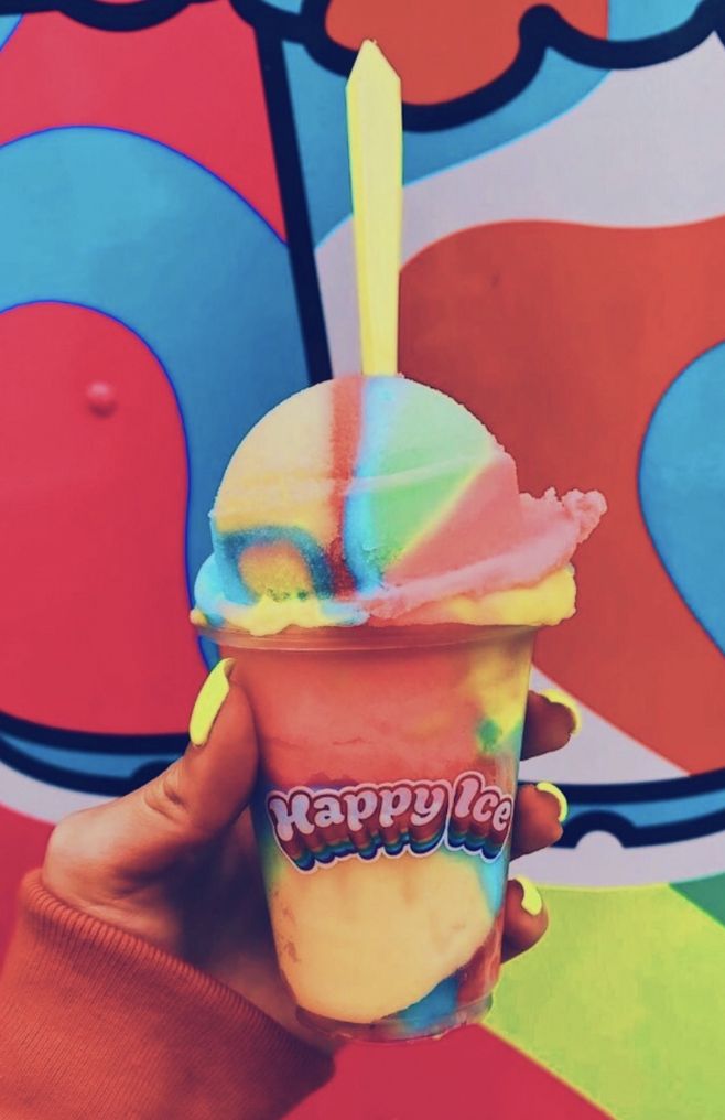 a hand holding an ice cream sundae in front of a colorful wall