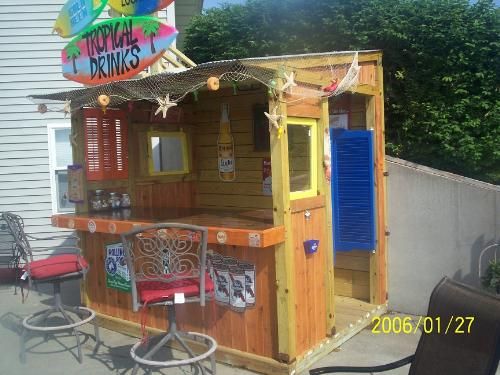 a small wooden bar with chairs around it on the back deck in front of a house