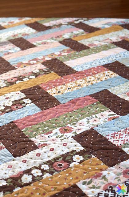 a close up of a quilt on a bed with brown and white flowers in the center