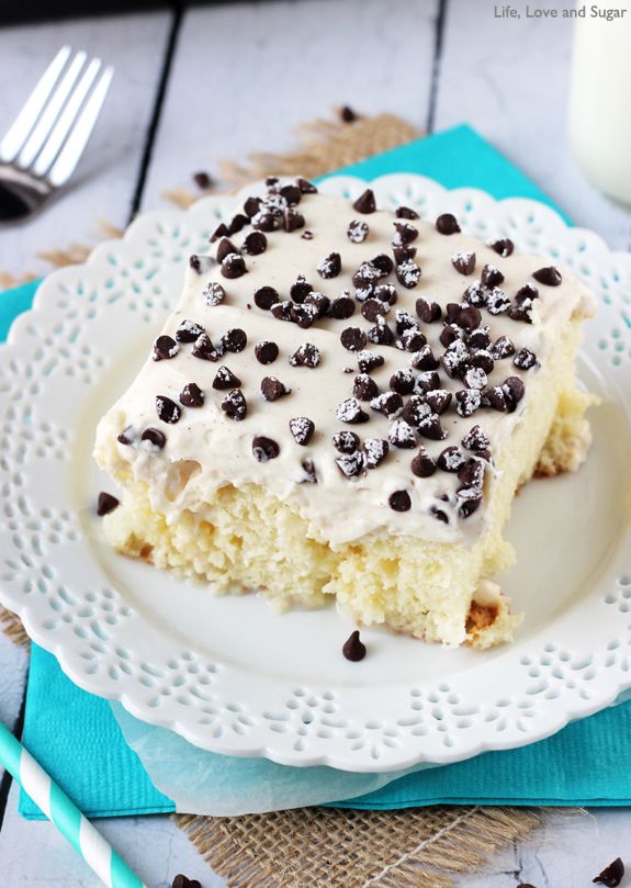 a white plate topped with a piece of cake covered in frosting and chocolate chips