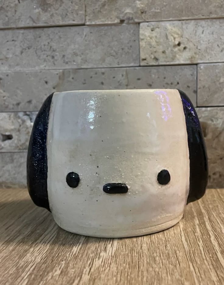 a white and black dog mug sitting on top of a wooden table next to a brick wall