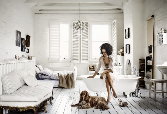 a woman sitting on a bathtub in a white bathroom with two dogs laying next to it